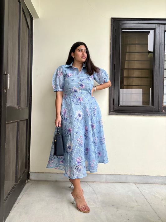 A woman wearing a blue floral shirt dress with a classic collar, balloon sleeves, and a flared hem.